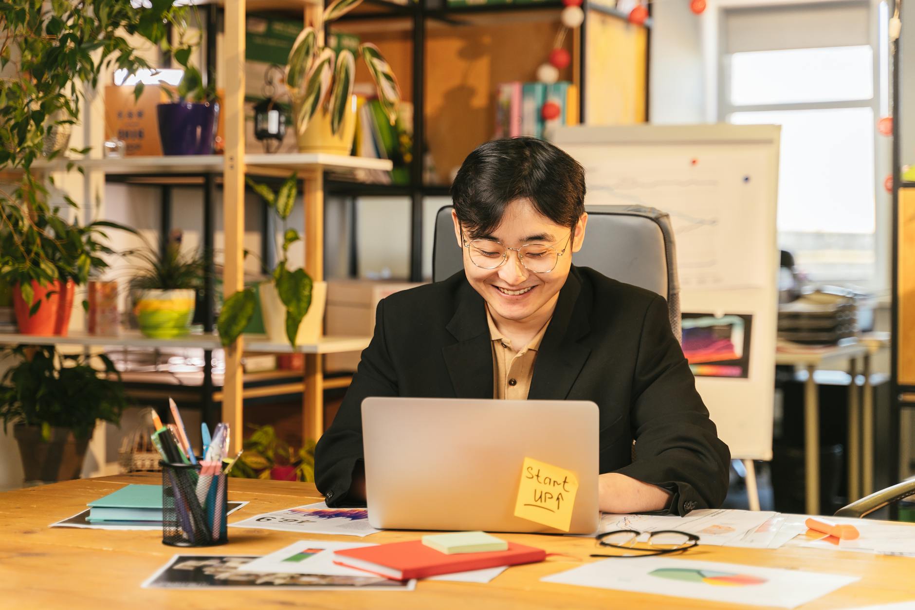 Uśmiechnięty pracownik w garniturze pracuje na laptopie przy biurku z roślinami