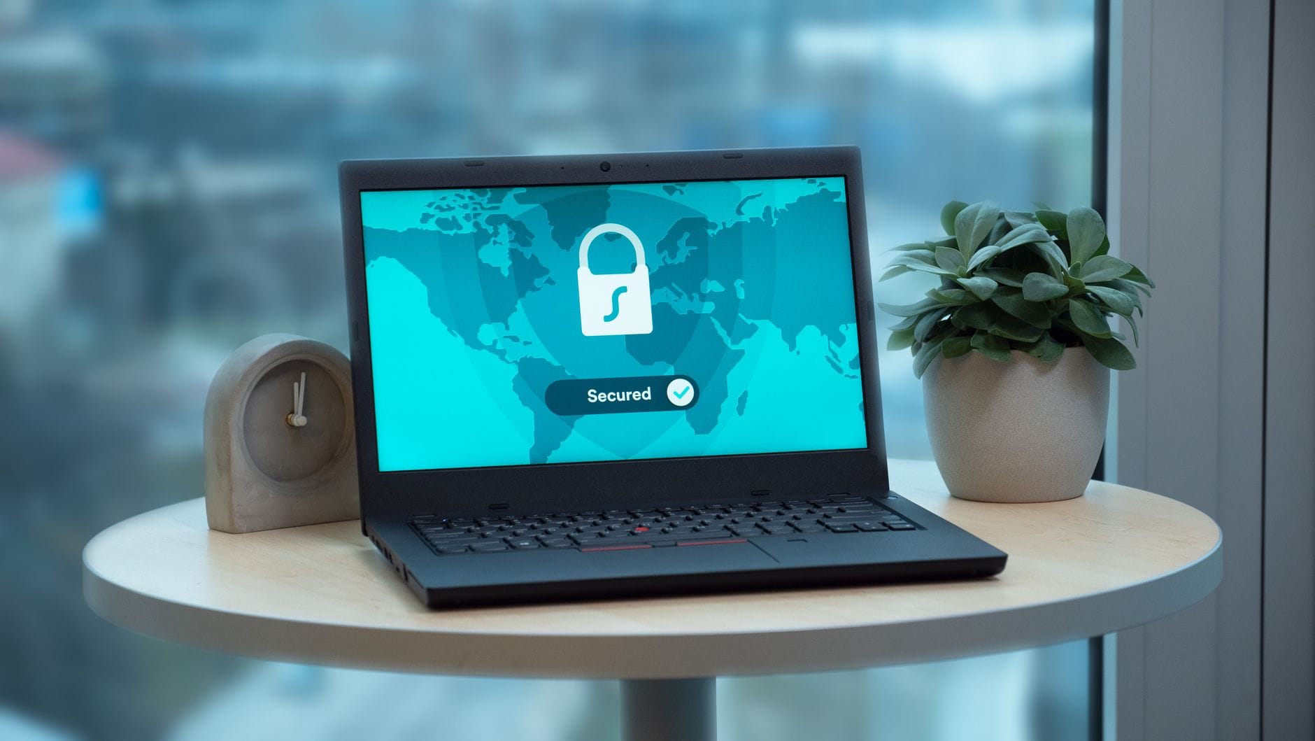 Laptop z ikoną kłódki na ekranie obok rośliny i zegara Laptop z ikoną kłódki na ekranie obok rośliny i zegara